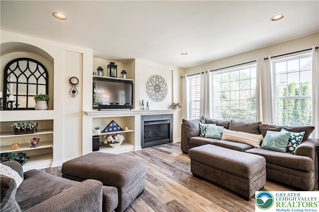 living room featuring wood finished floors, recessed lighting, built in features, and a glass covered fireplace