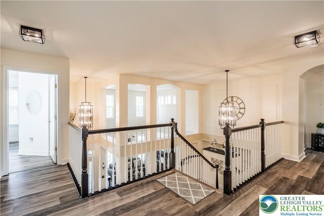 hallway featuring an upstairs landing, a chandelier, arched walkways, and wood finished floors