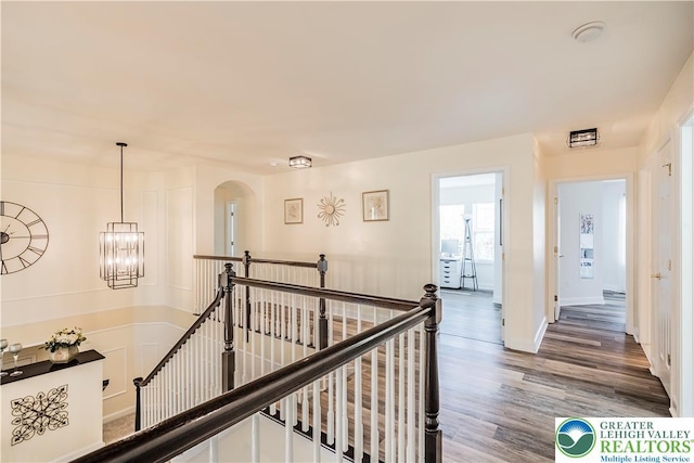 corridor with an upstairs landing, wood finished floors, baseboards, and a chandelier