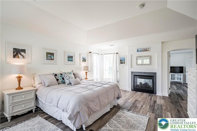 bedroom featuring dark wood finished floors, arched walkways, a multi sided fireplace, and baseboards