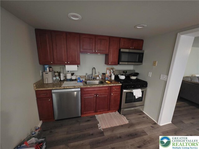 kitchen with stainless steel appliances, a sink, reddish brown cabinets, dark wood finished floors, and baseboards