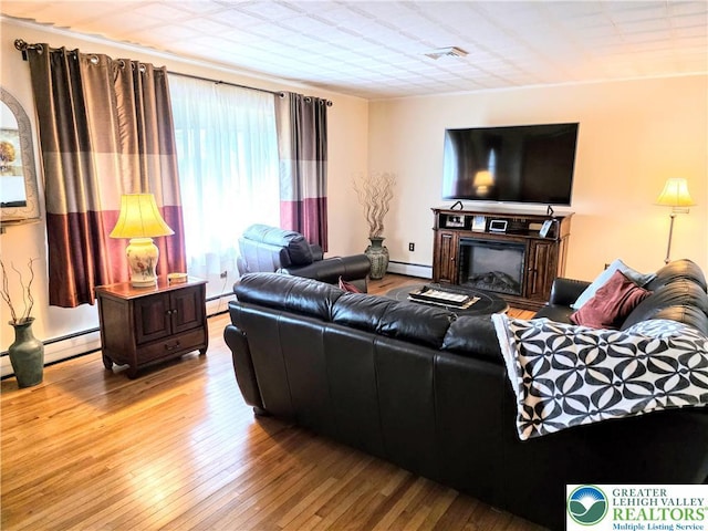 living area with hardwood / wood-style flooring, a baseboard heating unit, and a fireplace