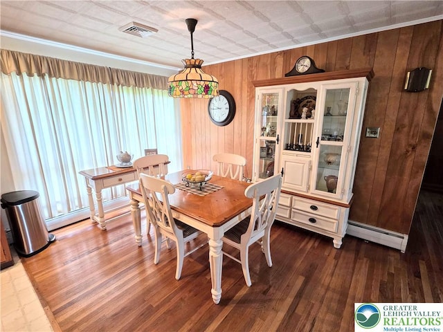 dining room featuring a baseboard heating unit, healthy amount of natural light, wood walls, wood finished floors, and crown molding
