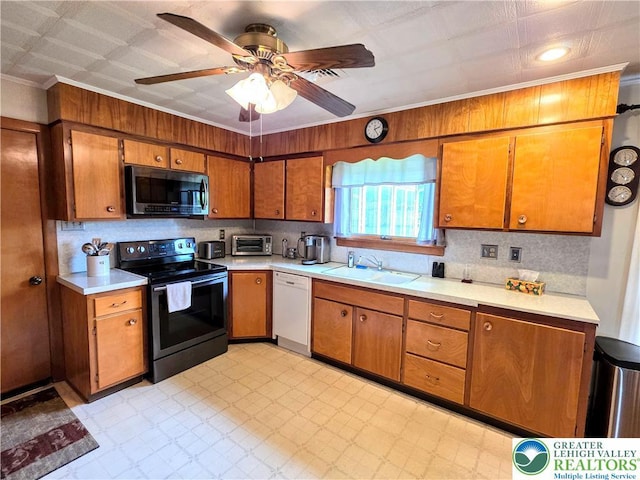 kitchen with appliances with stainless steel finishes, a sink, brown cabinets, light countertops, and ornamental molding