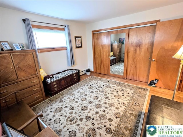 bedroom featuring wood finished floors, a baseboard heating unit, and a closet