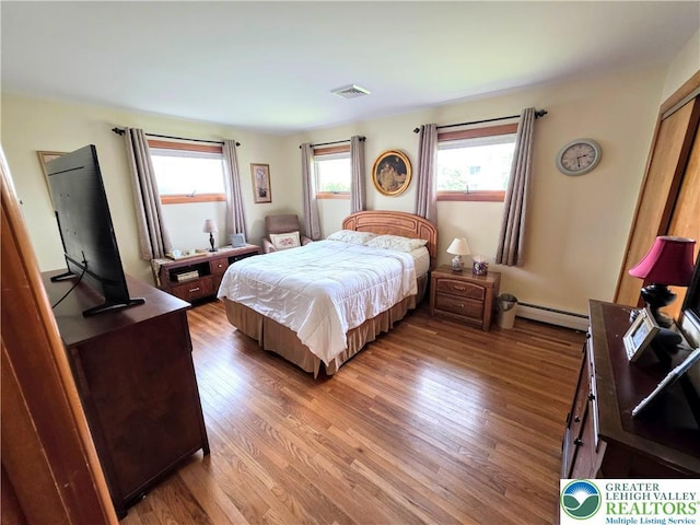 bedroom with a baseboard heating unit and wood finished floors