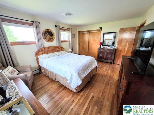 bedroom featuring light wood finished floors, a baseboard heating unit, and a closet