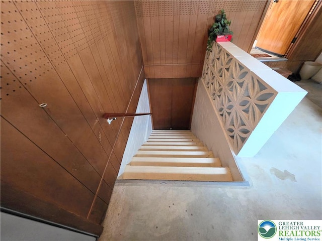 staircase with wood walls and concrete floors