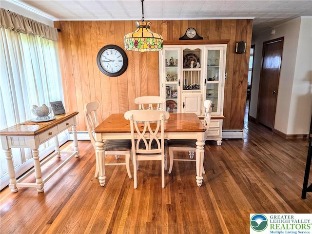 dining space featuring a baseboard radiator, crown molding, wood walls, baseboards, and wood finished floors