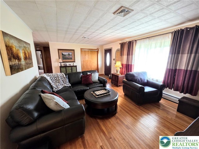 living area featuring baseboard heating, hardwood / wood-style floors, and crown molding