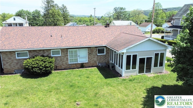 back of house featuring brick siding, a yard, a sunroom, and a shingled roof