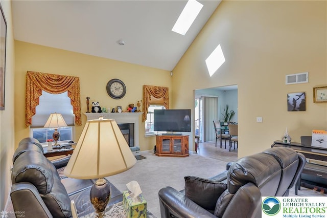 living room with a skylight, high vaulted ceiling, carpet, and a glass covered fireplace