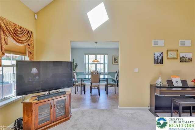 carpeted living area with a skylight, baseboards, high vaulted ceiling, and tile patterned floors