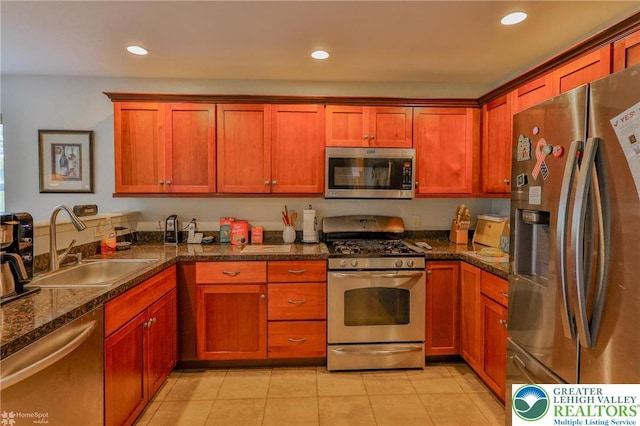kitchen with appliances with stainless steel finishes, a sink, recessed lighting, light tile patterned flooring, and dark stone counters