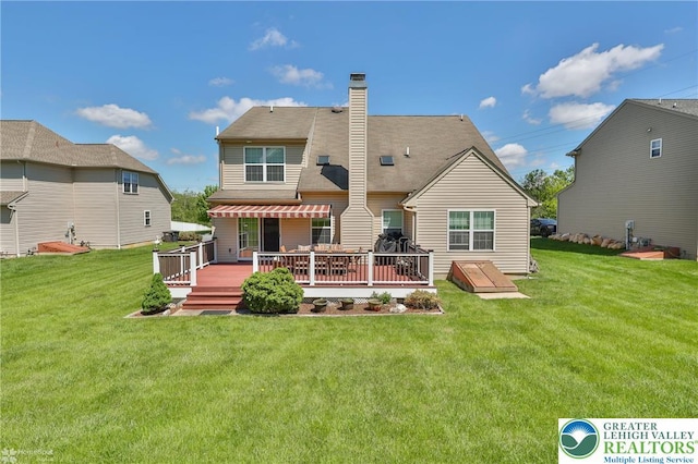 rear view of property featuring a deck, a chimney, and a yard