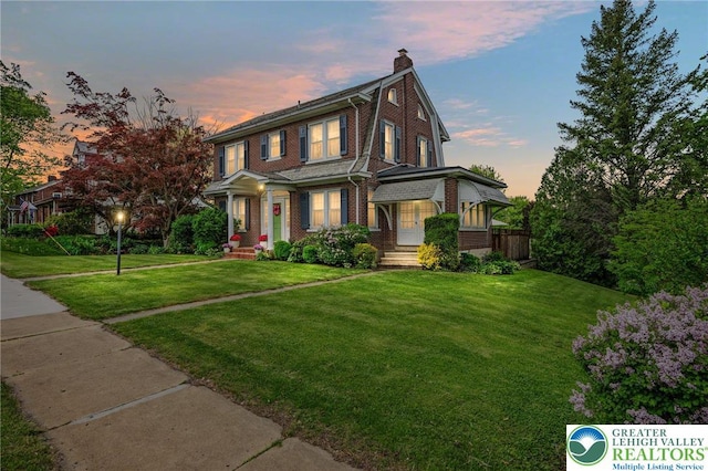 view of front of house with brick siding, a chimney, and a lawn