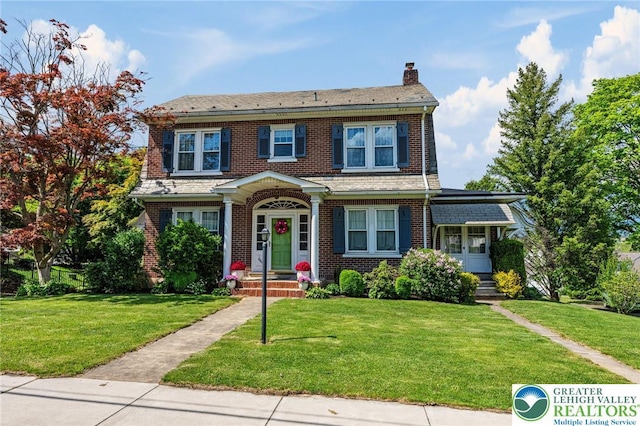 view of front of property with a chimney, a front yard, and brick siding