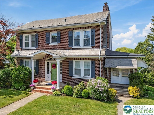 view of front of property featuring a chimney, brick siding, a front yard, and a high end roof