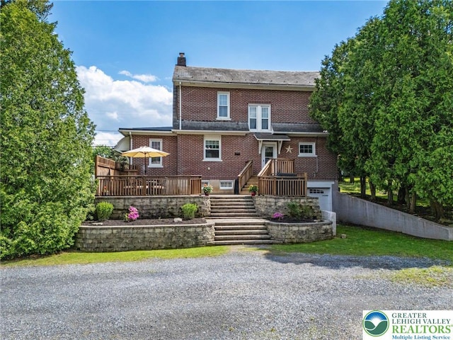 rear view of house with a chimney, brick siding, a wooden deck, an attached garage, and fence