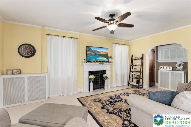 living room featuring arched walkways, a ceiling fan, a tile fireplace, crown molding, and radiator heating unit