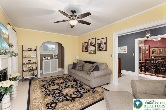 living room with ceiling fan, crown molding, arched walkways, a tile fireplace, and baseboards