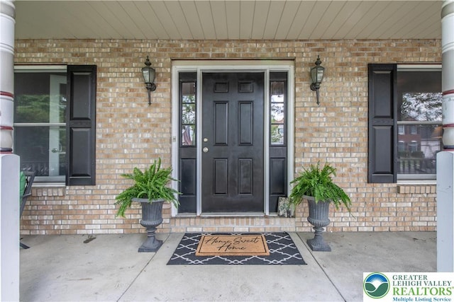view of exterior entry featuring brick siding and covered porch