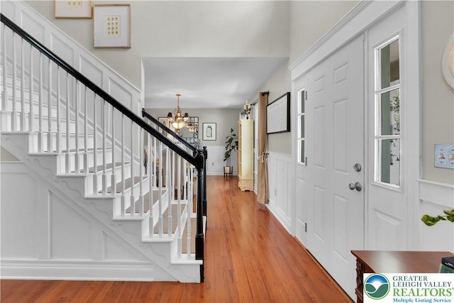 foyer entrance featuring a chandelier, stairway, wood finished floors, a decorative wall, and a wainscoted wall