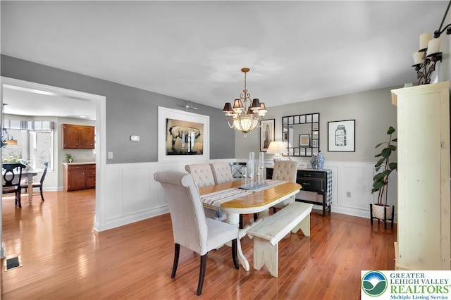 dining area with a chandelier, light wood-type flooring, wainscoting, and a decorative wall