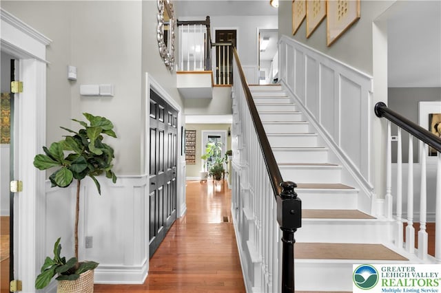 stairway featuring wood finished floors, wainscoting, and a decorative wall