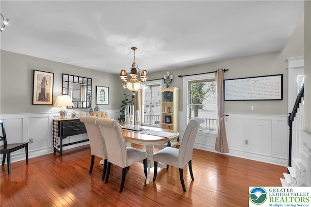 dining space with a chandelier, wood-type flooring, a decorative wall, wainscoting, and stairs