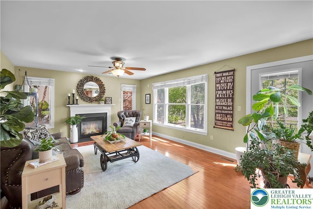 living area featuring a fireplace with flush hearth, baseboards, wood finished floors, and ceiling fan