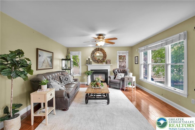 living area featuring wood finished floors, baseboards, a ceiling fan, and a glass covered fireplace