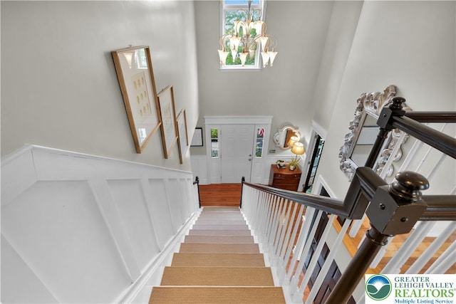stairway featuring a high ceiling, a chandelier, a wainscoted wall, and a decorative wall