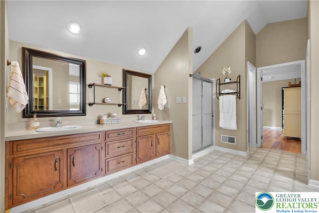 bathroom featuring lofted ceiling, a stall shower, baseboards, and double vanity