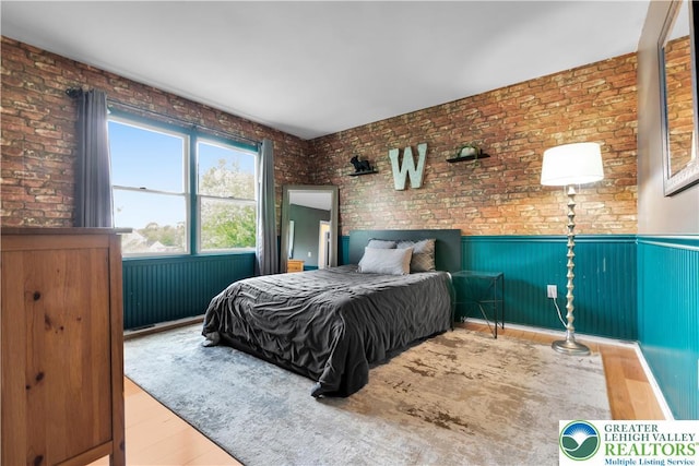 bedroom featuring wainscoting, brick wall, and wood finished floors