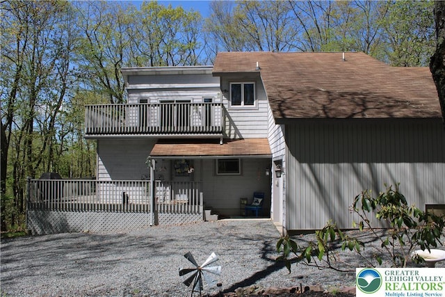 back of house featuring a balcony and roof with shingles