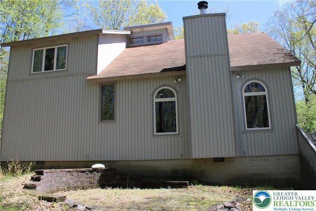 view of side of home featuring crawl space, a chimney, and roof with shingles