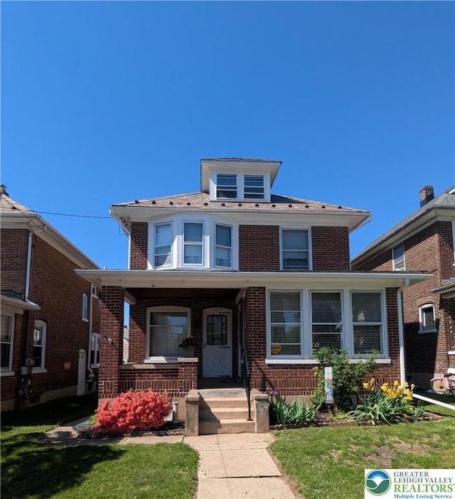 american foursquare style home with brick siding, covered porch, and a front yard