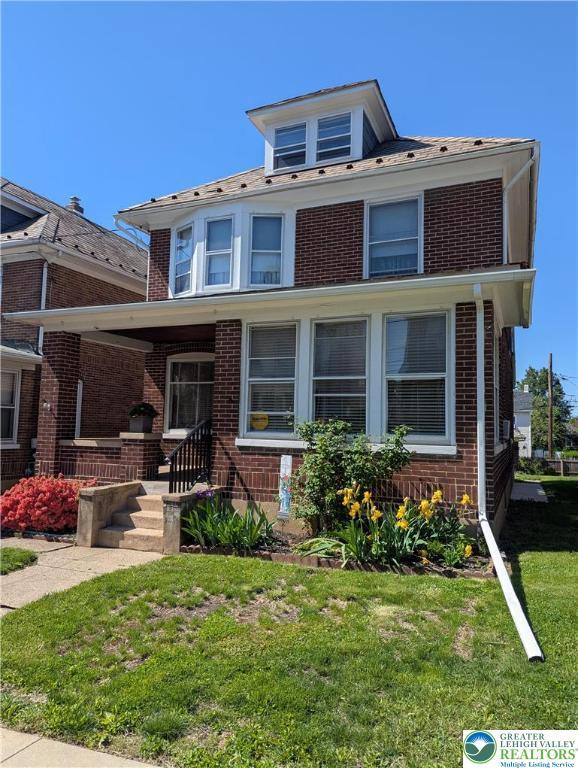 view of front of property with brick siding, a front lawn, and covered porch