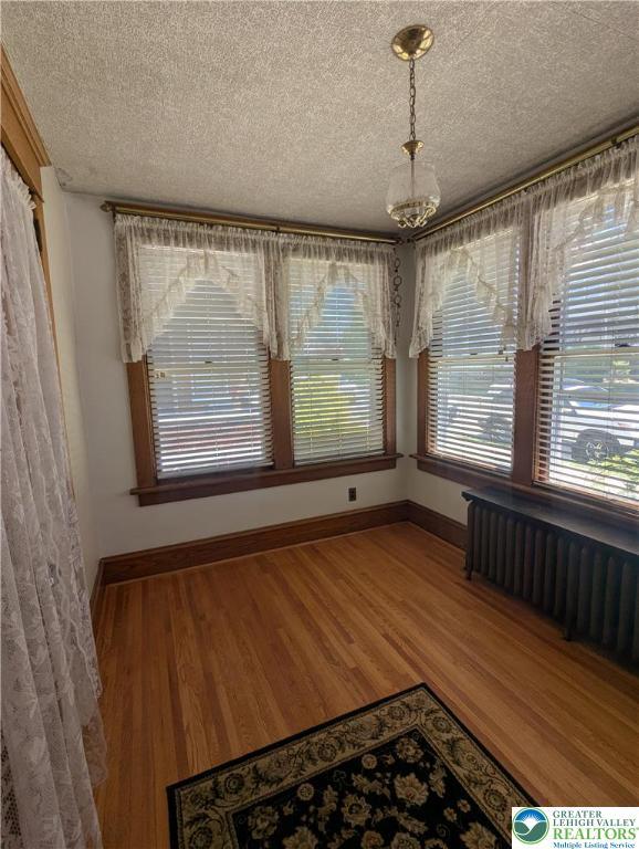 unfurnished dining area featuring radiator heating unit, a textured ceiling, wood finished floors, a chandelier, and baseboards