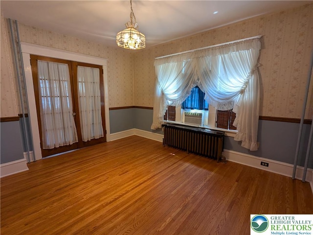spare room with radiator, wallpapered walls, wood finished floors, a chandelier, and cooling unit