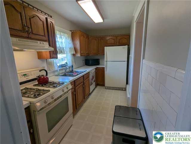 kitchen featuring white appliances, under cabinet range hood, a sink, light flooring, and light countertops