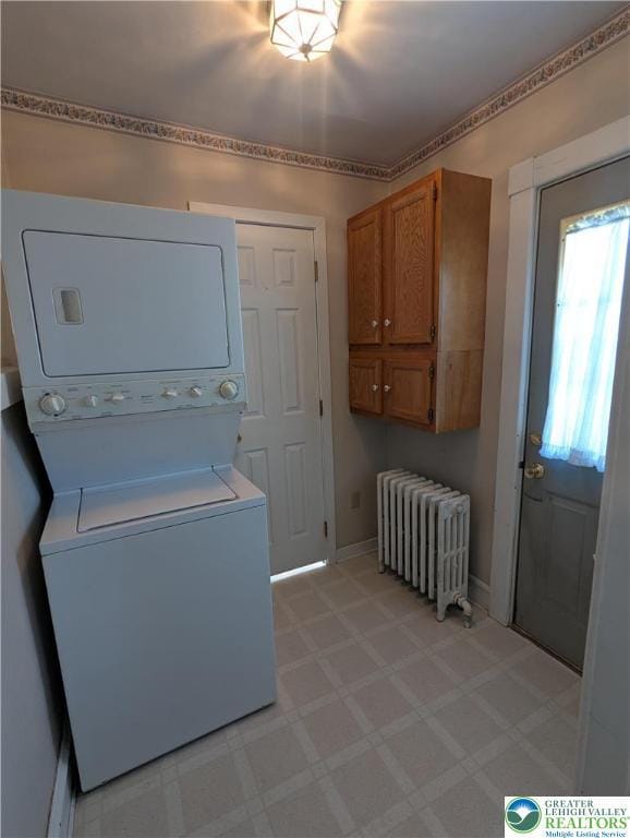 clothes washing area with radiator heating unit, stacked washing machine and dryer, and baseboards