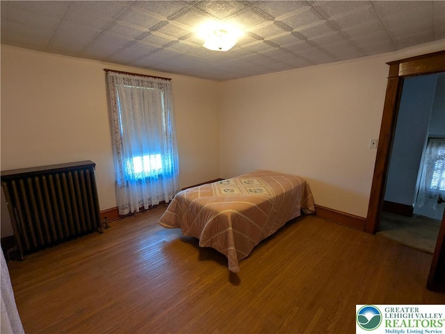 bedroom with radiator, wood finished floors, and baseboards
