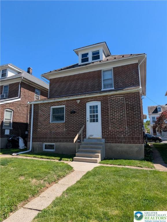 view of front of house with brick siding, entry steps, and a front yard