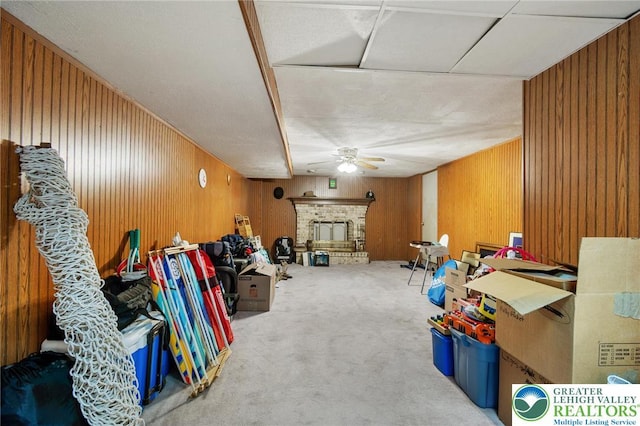 basement featuring wooden walls, a brick fireplace, a ceiling fan, and carpet flooring