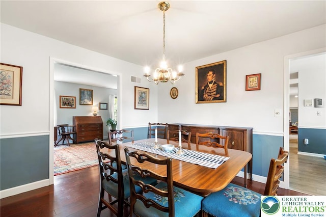 dining area with dark wood-type flooring, a chandelier, and baseboards