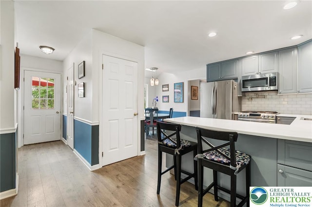 kitchen featuring stainless steel appliances, backsplash, light countertops, light wood-type flooring, and a peninsula