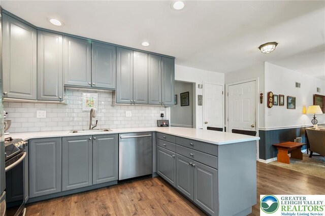 kitchen featuring appliances with stainless steel finishes, a sink, gray cabinetry, a peninsula, and dark wood-type flooring