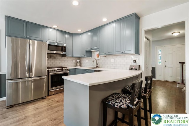 kitchen featuring stainless steel appliances, a peninsula, a sink, light wood finished floors, and light countertops
